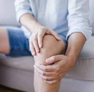 Man suffering from knee pain sitting sofa